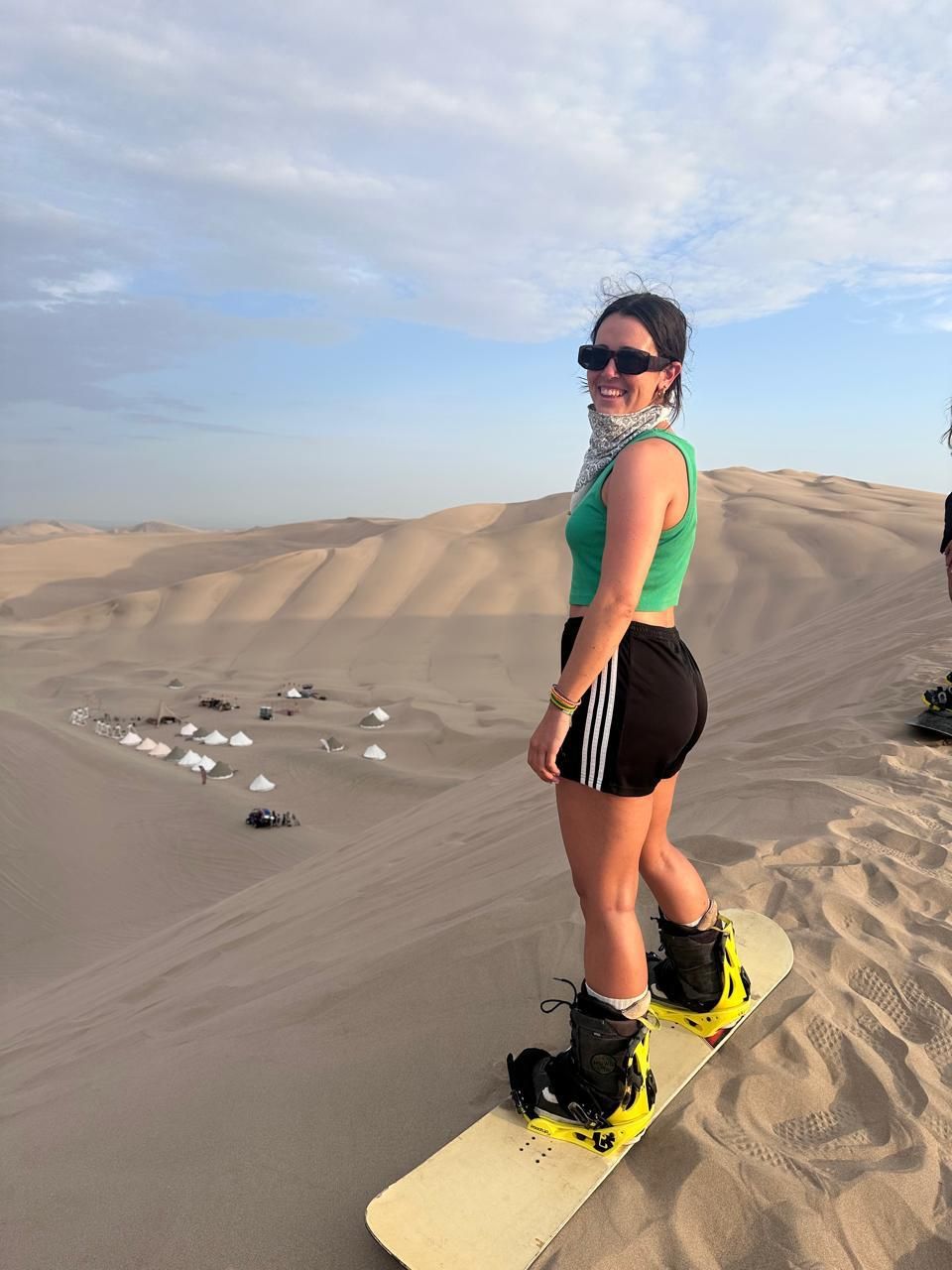 Viajera con tabla de sandboard en la cima de una duna